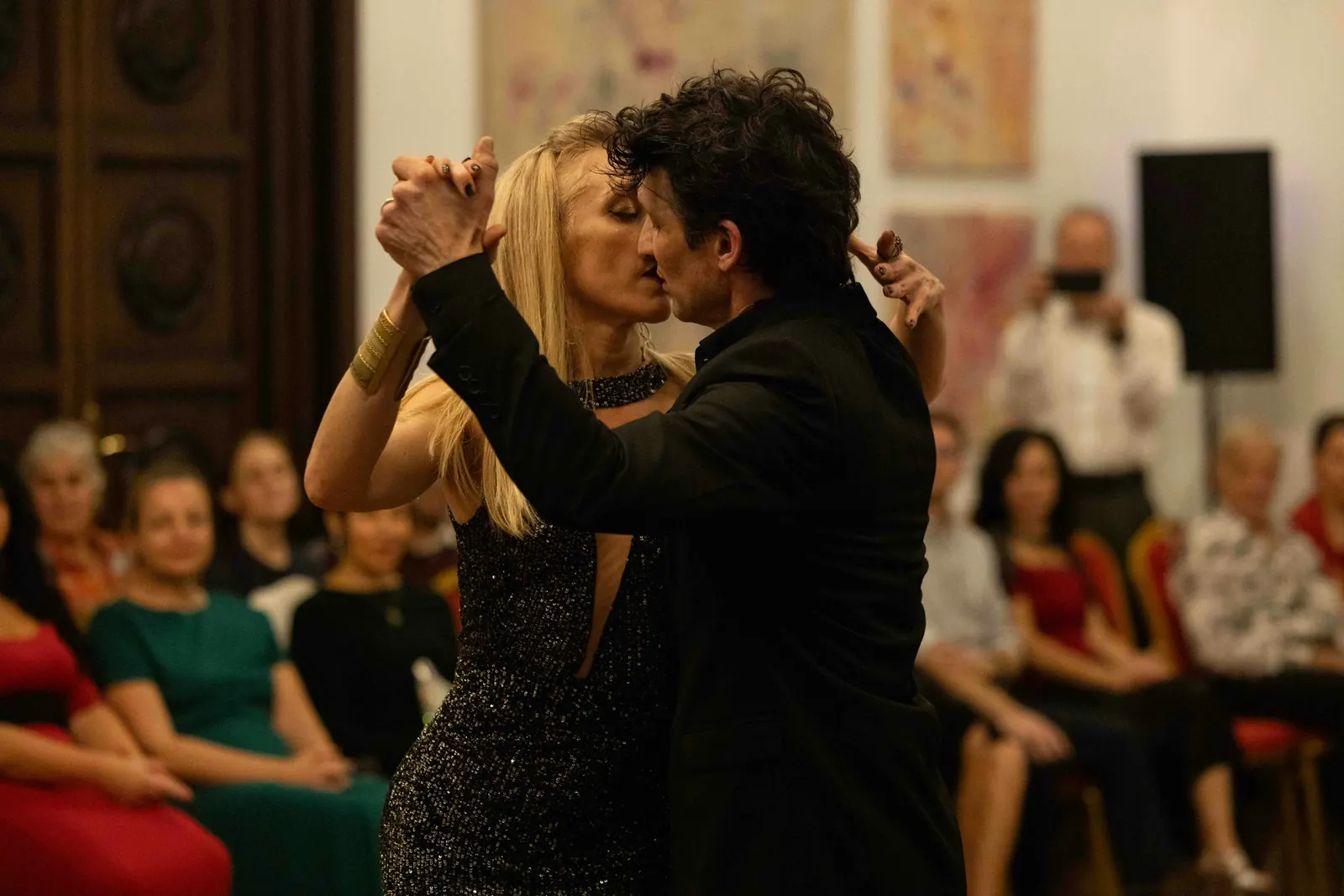 A tango couple in close embrace dancing in front of seated guests, the woman's eyes closed