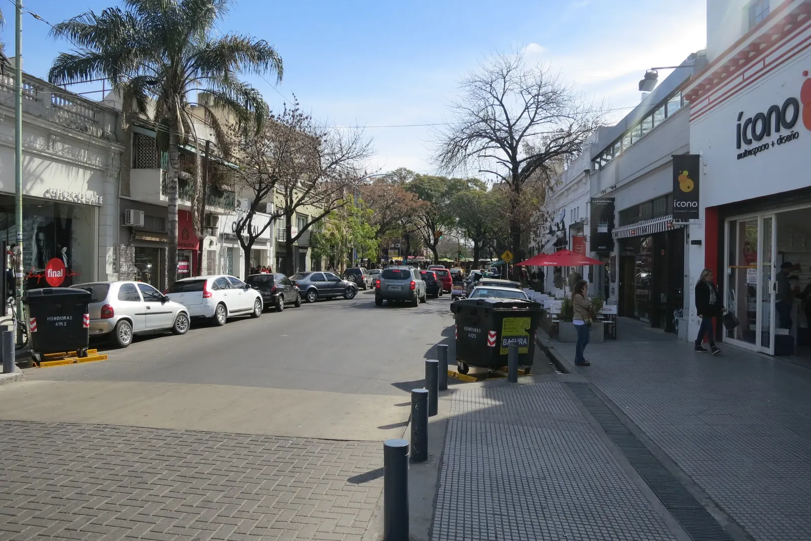 A tree-lined street in Palermo Soho with shops on both sides, cobbled paving and parked cars
